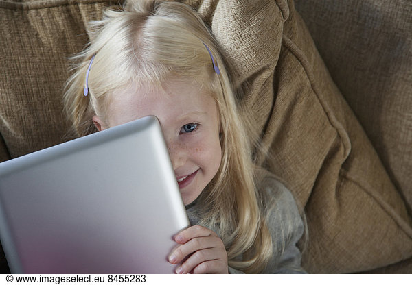 A young girl holding a silver laptop in front of her face.