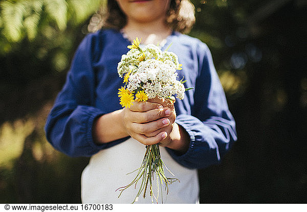 A young girl holds a bunch of wild flowers in a farm paddock