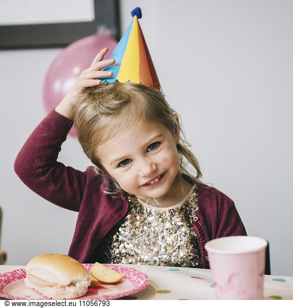 A young girl in a party hat at a birthday party.