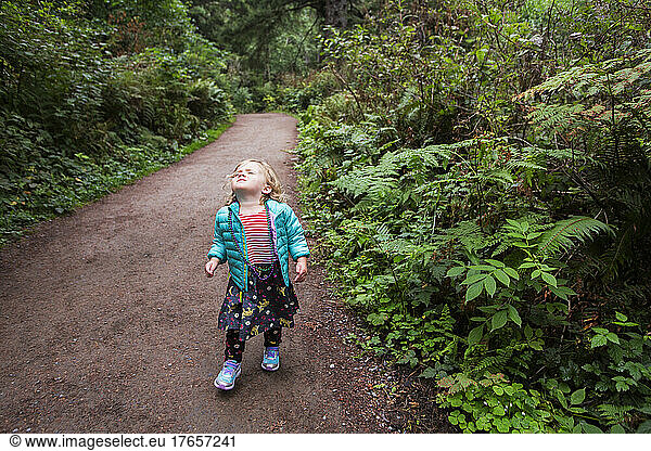 A young girl looks up  eyes closed on forested trail