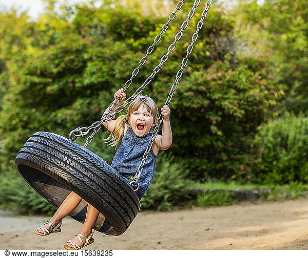 A young girl makes a silly face as she swings on a tire swing; Edmonton  Alberta  Canada