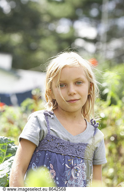 A young girl sitting in among the fresh green foliage of a garden. Vegetables and flowers. Picking fresh vegetables.