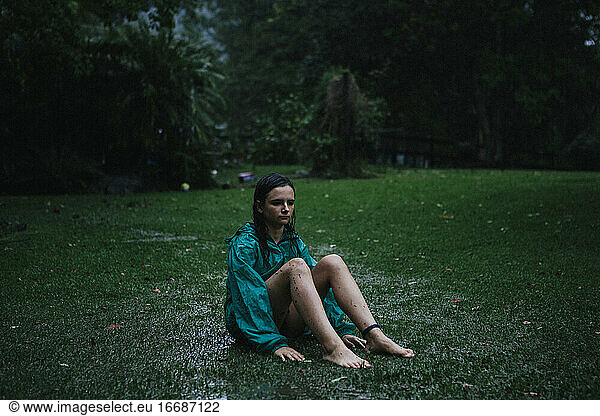 A young girl sitting on the grass in the rain during a tropical storm