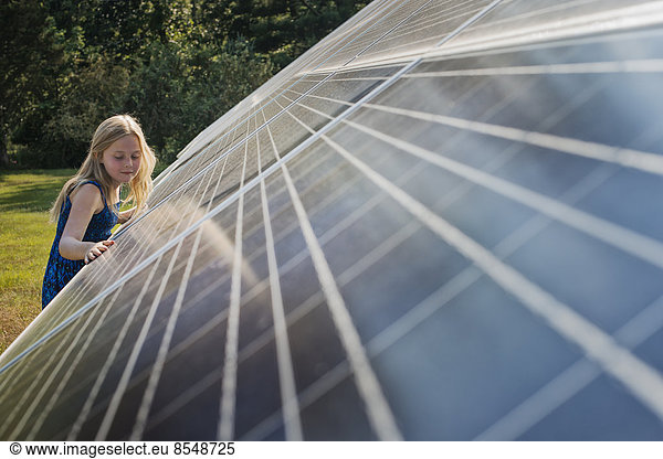 A young girl standing beside and leaning against a large solar panel installation.