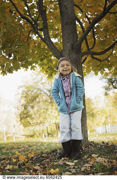 A young girl standing under a tree  on a farm. Autumn foliage.