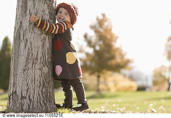 A young girl with her arms around a tree in autumn sunshine