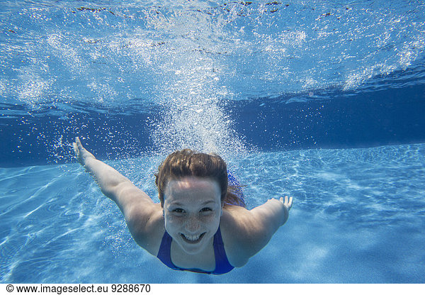 A young girl with long hair fanning out in the water  swimming underwater.