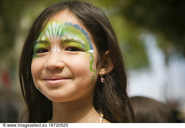 A young girl with painted face at a parade in Santa Barbara. The parade features extravagant floats and costumes.