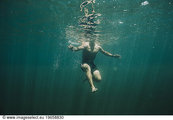A young hispanic male swims to the lake's surface.