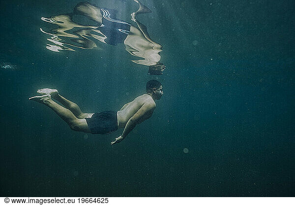 A young male floats freely underwater in a lake.