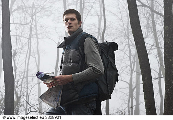 A young male hiker holding a map in a misty forest
