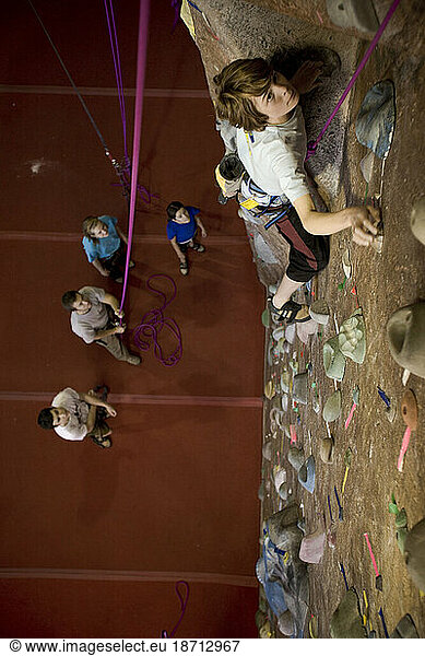 A young male teen rock climber top ropes at a rock climbing gym.