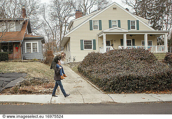 A young man carries his sister piggy back down a suburban sidewalk