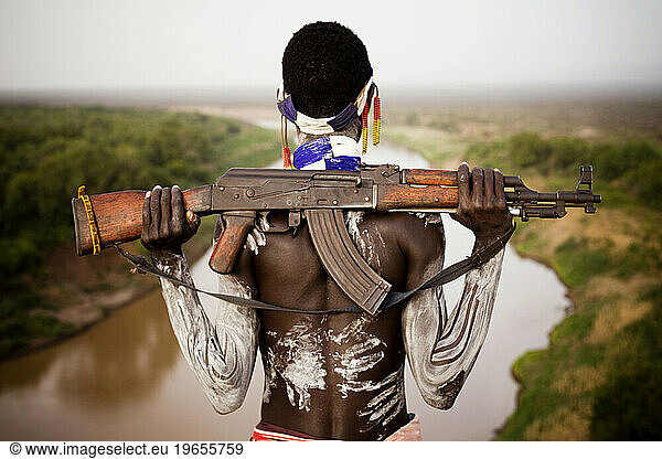 A young man holds his kalashnikov rifle while overlooking the Omo river in the remote Omo Valley of Ethiopia