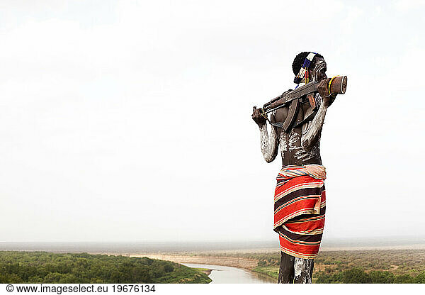 A young man holds his kalashnikov rifle while overlooking the Omo river in the remote Omo Valley of Ethiopia