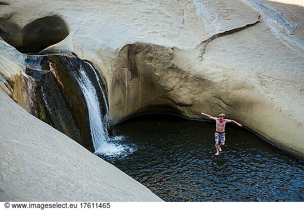A young man jumps into a pool at the Seven Teacups in the Sierra Nevada mountains.