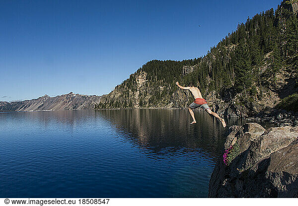 A young man jumps into the cold  clear waters of Crater Lake.