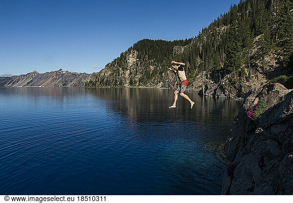 A young man jumps into the cold  clear waters of Crater Lake.