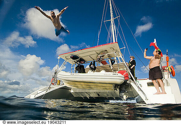A young man jumps off the swim platform of a catamaran while on a family sailing vacation in the British Virgin Islands