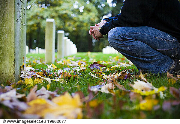 A young man kneels as he reads one of the many tombstones decorated with autumn leaves at Fort Lawton Cemetery in Seattle  WA.