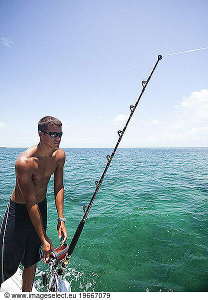 A young man lets fishing line out of his reel while deep sea fishing in Belize.