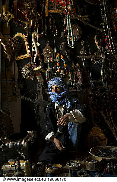 A young man sits on the floor of his store surrounded by his beads  mirrors  knives and silver which he sells to passing tourists in Morocco.