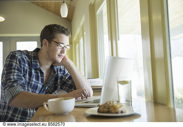 A young man sitting at a table using a laptop computer.