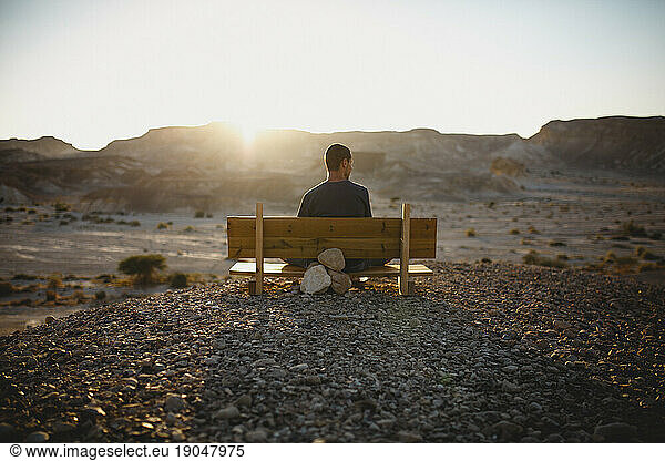 A young man sitting on a bench watching the desert in sunset
