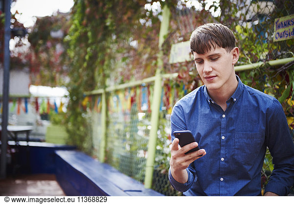 A young man sitting outdoors looking down at a cellphone.