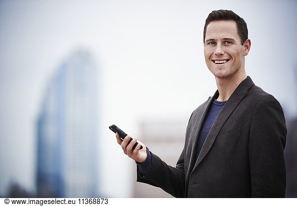 A young man standing on a rooftop holding a cellphone.
