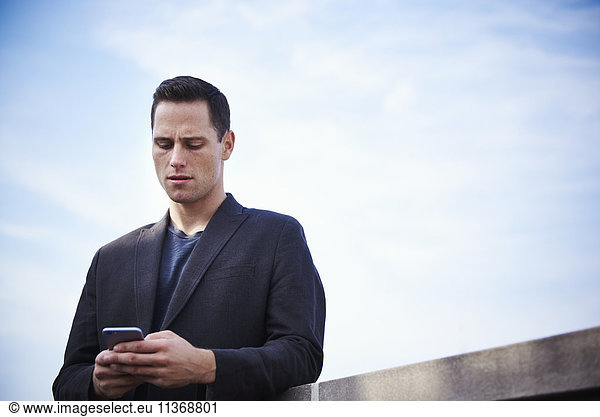 A young man standing on a rooftop looking at a cellphone.