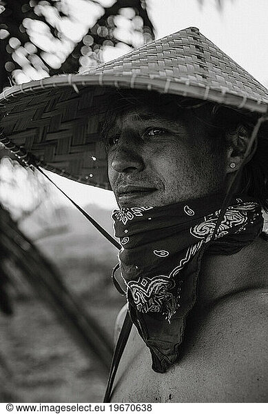 A young man wearing an Asian cone hat in rice fields at sunset. Bali.