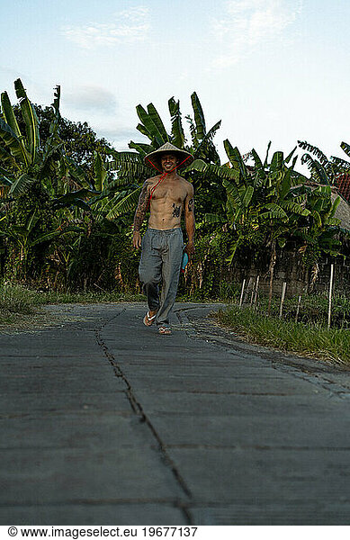 A young man wearing an Asian cone hat in rice fields at sunset. Bali.