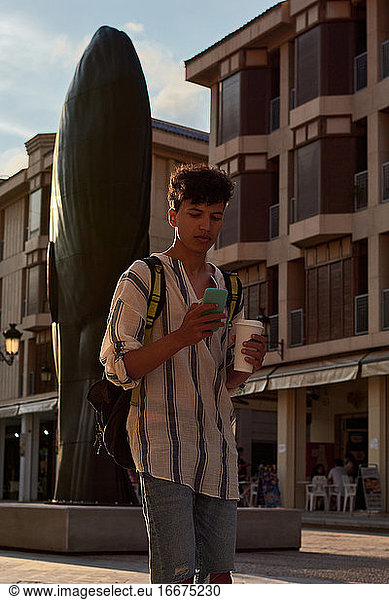 A young man with afro hair walks at sunset while using his cell phone