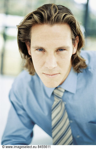 A young man with curly brown hair wearing a blue shirt and tie.