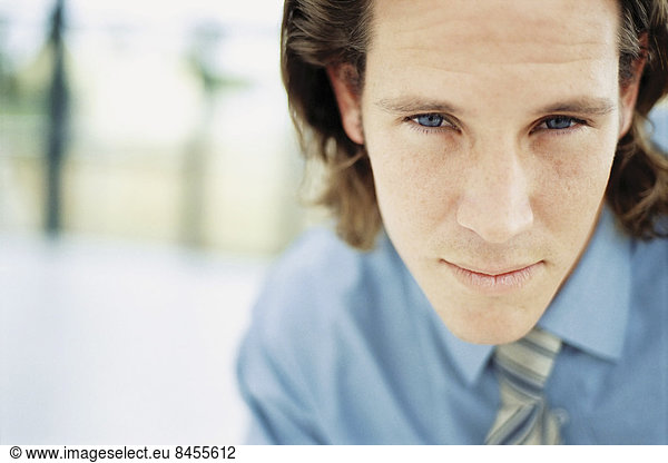 A young man with curly brown hair wearing a blue shirt and tie.