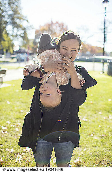 A young mother playfully holds her toddler daughter upside down.