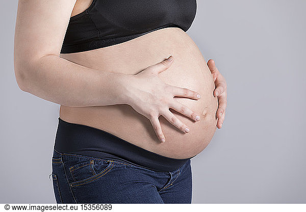A young pregnant woman holding her belly in a studio against a light background; Edmonton  Alberta  Canada