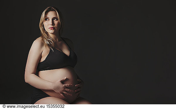 A young pregnant woman holding her belly in a studio and looking away from the camera thinking about her unborn child: Edmonton  Alberta  Canada