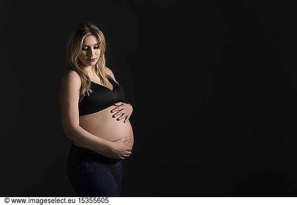 A young pregnant woman holding her belly in a studio and looking down at her unborn child; Edmonton  Alberta  Canada