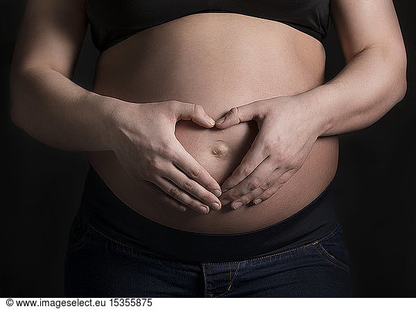 A young pregnant woman holding her belly in a studio and making a heart shape over her unborn child; Edmonton  Alberta  Canada