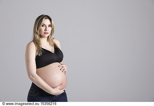 A young pregnant woman holding her belly in a studio and posing for the camera; Edmonton  Alberta  Canada