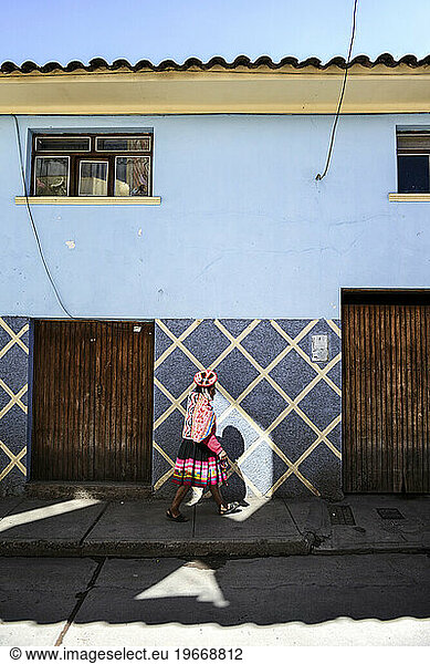A young Quechuan woman walks into a lone sunny spot on a shady street in Urubamba.