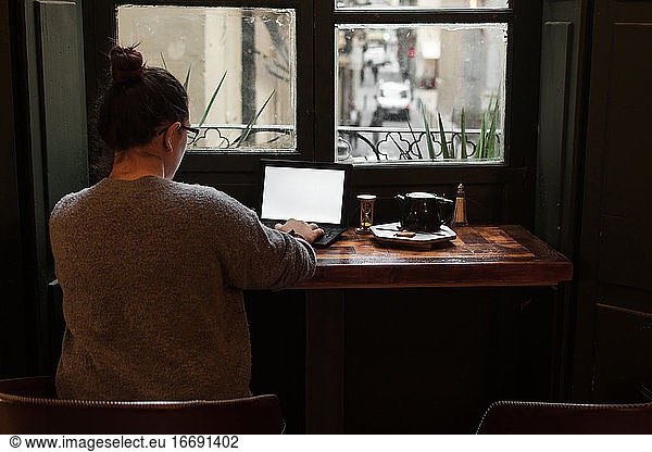 A young student works on a table near a pub window
