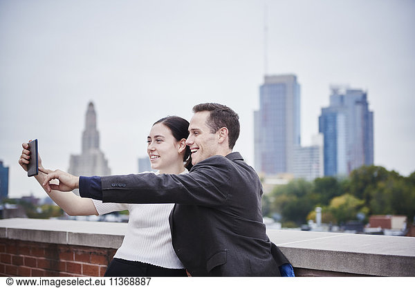 A young woman and a young man standing on a rooftop looking at a cellphone together.