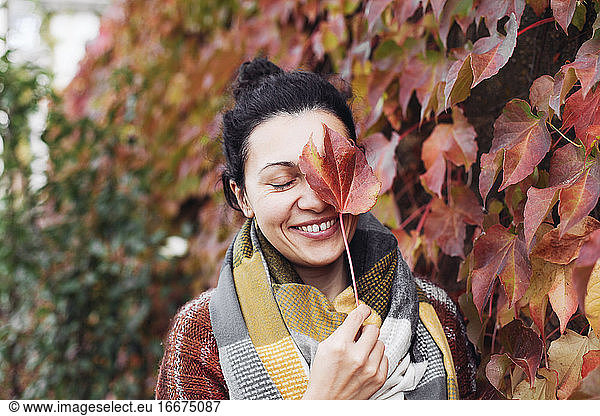 A young woman covers her face with a red leaf and laughing tr