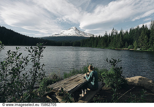 A young woman eats lunch at picnic table next to a lake near Mt. Hood.