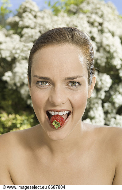 A young woman holding a strawberry between her teeth.