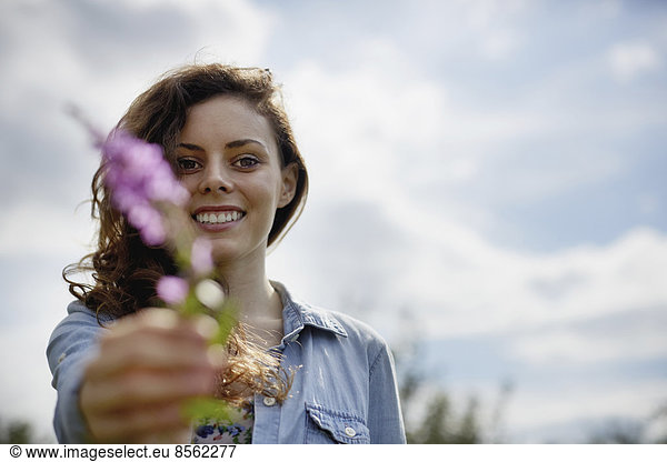 A young woman holding out a wild flower with pink petals.