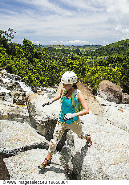 A young woman hops between boulders while exploring a river on a sunny day in Puerto Rico.